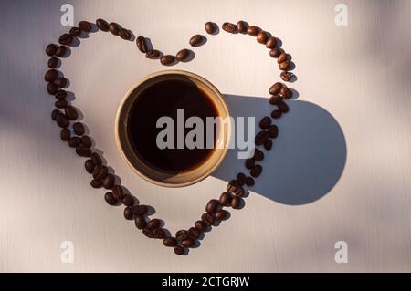 Blick von oben auf eine Tasse Kaffee umgeben von Kaffee Bohnen bilden ein Herz Stockfoto