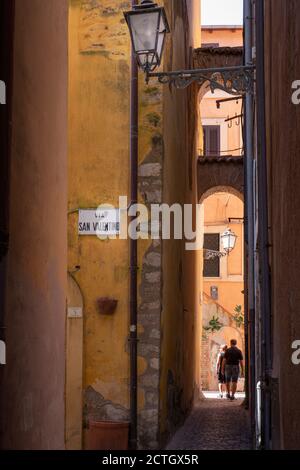 Ein Paar (Mann und Frau) spaziert durch die engen Gassen von Terracina, Latina (Italien). Via San Valentino Plakette im Vordergrund. Stockfoto