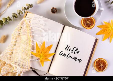 Herbstblätter, Tasse Kaffee, Buch lesen warmen Schal und geöffnetes Buch auf dem Tisch mit Text Hallo Herbst. Herbst- und Herbstkonzept. Stockfoto