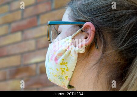 Nahaufnahme des kleinen Mädchens Gesicht trägt hübsche Stoff Gesichtsmaske draußen, vor einem Backstein Wand Hintergrund in der Sommersonne Stockfoto