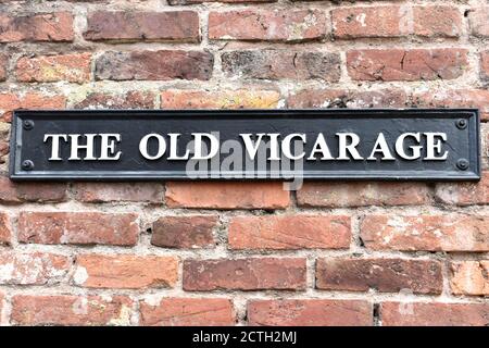 Nahaufnahme des alten Pfarrvikarage Zeichen weißen Text auf Schwarze Metall-Plakette vor Backstein Wand Hintergrund außen Stockfoto
