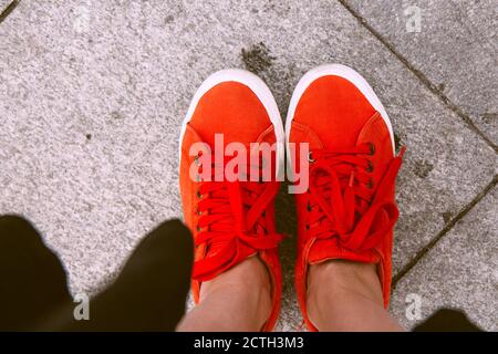 Weibliche Füße von oben gesehen. Selfie für jeden Einsatz. Fuß und Beine in roten Sneakers. Fuß steht auf den grauen Fliesen. Mit Kopierbereich. Füße außerhalb in der Nähe U Stockfoto