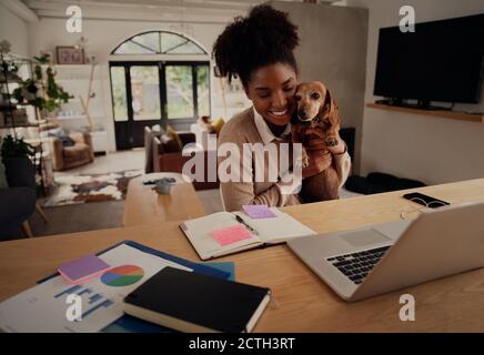 Junge afrikanische Frau umarmt Haustier Hund während der Arbeit auf Laptop Zu Hause