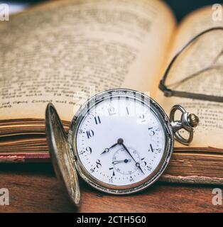 Vintage Taschenuhr und offenes altes Buch auf einem hölzernen Büroschreibtisch Hintergrund, Nahaufnahme. Zeit, Wissenschaftskonzept Stockfoto