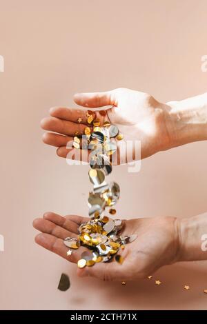 Menschliche Hände mit herabfallendem Konfetti auf einem rosa Hintergrund. Festliches Konzept. Stockfoto