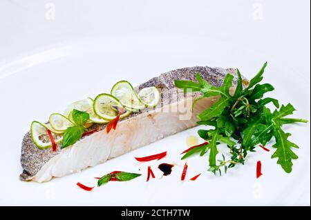 Gegrilltes Filet mit köstlichem weißen Fisch, verziert mit Zitronenscheiben Und frische grüne Rucola Salat Gemüse isoliert auf weißem Teller Stockfoto