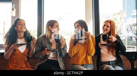 Weibliche Freunde sitzen im Café mit einer Tasse Kaffee und lächeln. Eine Gruppe von vier Frauen, die zusammen in einem Café Kaffee trinken. Stockfoto