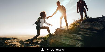 Frau, die Freund beim Wandern auf den Felsen klettern hilft. Teamarbeit von zwei Wanderinnen, die sich auf dem Bergsteigen gegenseitig helfen. Stockfoto