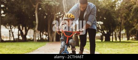 Jungen lernen, ein Fahrrad mit seinem Vater im Park zu fahren. Vater Lehre seinen Sohn Radfahren im Park. Stockfoto