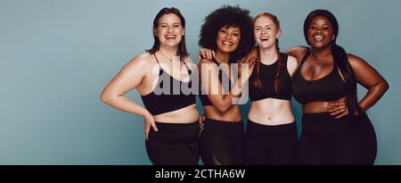 Porträt der Gruppe von Frauen zusammen posieren in Sportkleidung auf grauem Hintergrund. Multirassischen Frauen mit unterschiedlicher Größe zusammen suchen Stockfoto