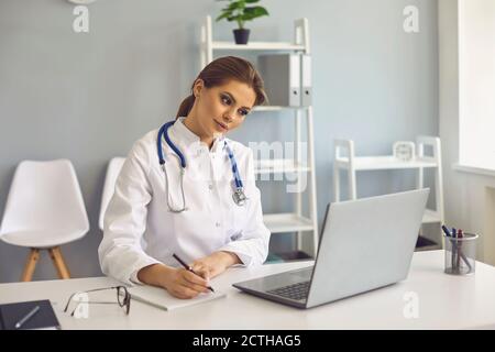 Ärztin macht sich Notizen während einer Online-Lektion oder einem Videoanruf Beratung in der medizinischen Klinik Stockfoto