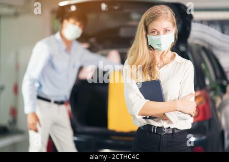 Der Taxifahrer in der medizinischen Maske setzen gelbe Koffer von Frauen in den Kofferraum eines Autos. Lebensstile und Transportkonzepte der Menschen. Stockfoto