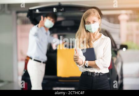 Der Taxifahrer in der medizinischen Maske setzen gelbe Koffer von Frauen in den Kofferraum eines Autos. Lebensstile und Transportkonzepte der Menschen. Stockfoto