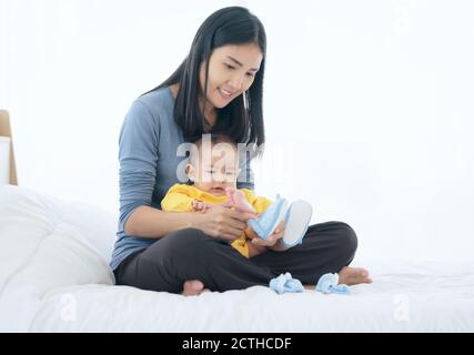 Liebevolle Mutter Schuhe auf Baby auf Sofa zu Hause Stockfoto