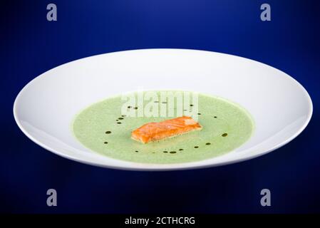 Grüne Spinatpüree-Suppe mit Lachsscheiben. Flach Lay Draufsicht auf einer weißen Platte auf einem blauen Hintergrund. Stockfoto