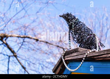 Handgemachte Krähe, Rabe oder Elster auf dem Dach. Der Vogel besteht aus schwarzem Draht und Schmuck (Perlenkette). Es sitzt auf Dachschindeln mit blauen si Stockfoto