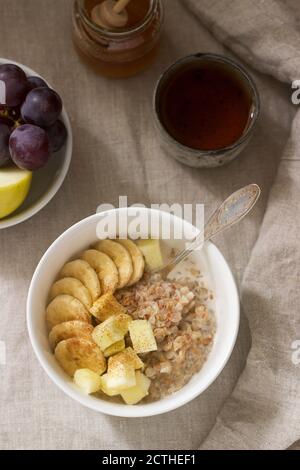 Buchweizenbrei mit Obst, grünem Tee, Obst und Honig auf einer Leinentischdecke. Rustikaler Stil. Stockfoto