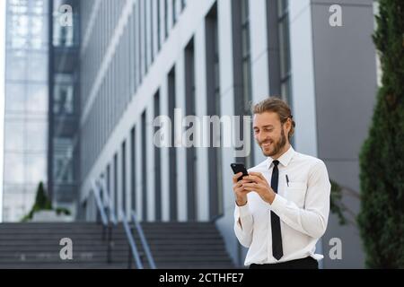 Porträt eines erfolgreichen jungen Geschäftsmannes. Ein lockiger Mann in einem weißen Hemd mit Telefon vor dem Hintergrund eines modernen Business-Centers Stockfoto