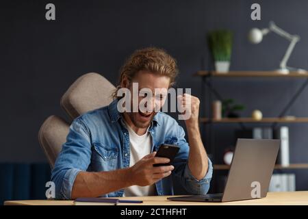 Junge gutaussehende langhaarige lockige Mann arbeitet im Büro mit Laptop und zum Ausdruck Positivität. Glücklicher Geschäftsmann bekam positive News.rewarded, neu Stockfoto