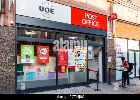 Eine Person in einer Gesichtsmaske wartet auf ein Postamt in der Camden High Street und beobachtet soziale Distanzierung während der Coronavirus-Pandemie, London, Großbritannien Stockfoto