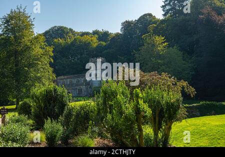 St. Peter-Kirche mit Bäumen im Hintergrund und Hecken im Vordergrund an einem sonnigen Tag. Stourton, Warminster, England. Stockfoto