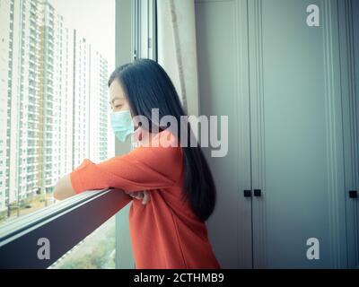Eine Frau mit einer Maske im Raum und stehen Blick aus dem Fenster Stockfoto