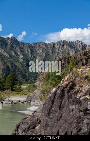 Eine Nahaufnahme einer Bergkette mit braunen und grauen Felsklippen mit grünen Bäumen und Gras im Altai mit Blick auf die Straße mit Zäunen von oben. Stockfoto