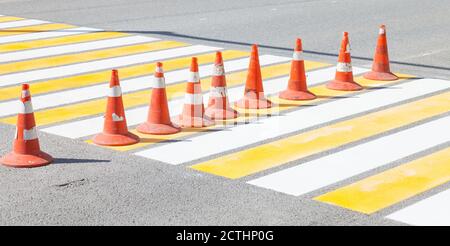 Fahrbahnmarkierungen Kegel von orange und weiß auf der zebraüberquerung des Fußgängerübergangs zum Schutz des Verkehrs auf frisch Aufgetragen Farbe auf das Grau Stockfoto