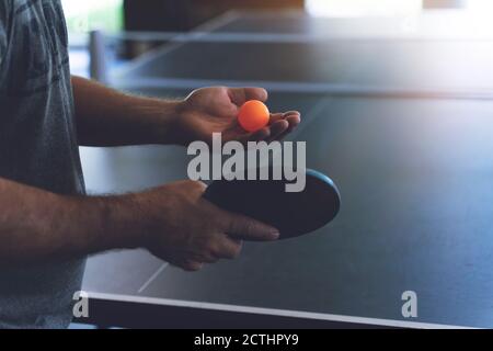 Ein junger Mann spielt Tischtennis. Er hält einen Ball und einen Schläger in den Händen Stockfoto