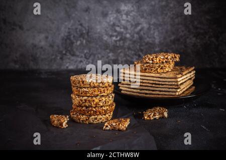 Karamell Erdnuss spröde aus Sonnenblumenkernen und Sesam und Fitness-Cookies mit Leinsamen auf dunkelschwarzem Beton Hintergrund. Stockfoto