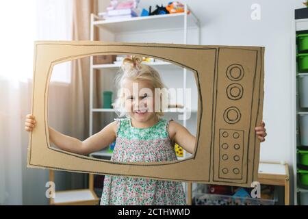 Fröhliches Kind spielt mit Karton-tv zu Hause. Zukunft Traum Beruf Konzept Stockfoto