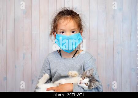 Nahaufnahme des Gesichts 5-jähriges Mädchen trägt eine schützende medizinische Maske Blick auf die Kamera, ein europäisches Kind mit einem Kätzchen verhindert ein ovid-19 Stockfoto