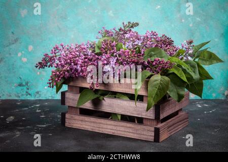 Lila Flieder Blumen Bouquet auf Holzkiste auf schwarzem Beton Hintergrund. Stilvolle Grußkarte mit Blumenmuster. Alles gute zum Muttertag. Stockfoto