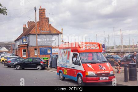 Blick auf einen Eiswagen, der am Maldon Quayside geparkt ist, ein Junge, der Eiscreme isst, sitzt auf einer Bank und am Flussufer mit Queens Head Pub im Hintergrund. Stockfoto