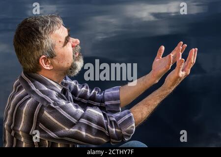 Ein älterer Mann fragt den Wind vom Himmel und sitzt am Meer Stockfoto