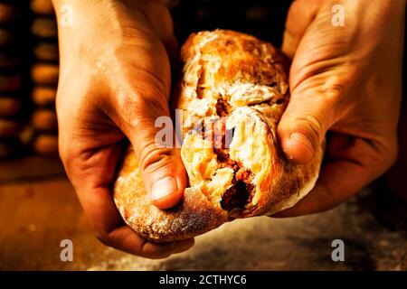 Die Hände des Kochs brechen den indischen Naan. Ein orientalisches Fladenbrot, gefüllt mit Fleisch in den Händen eines Mannes. Pita gefüllt mit Fleisch in den Händen von einem m Stockfoto