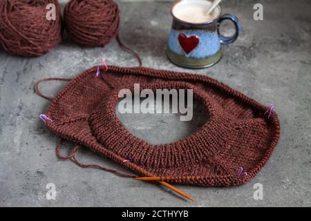 Brauner Pullover, Strickverfahren, mit Keramik-Tasse mit rotem Herz auf Beton Hintergrund Stockfoto