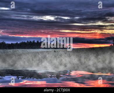 Fantastischer Sonnenuntergang über dem Feld, der sich im nebligen See spiegelt. HDR Stockfoto