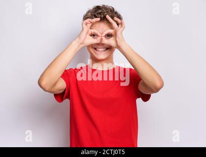 Portrait von schönen Teenager Junge macht OK Geste mit Hand auf Augen durch die Finger schauen. Glücklich lächelndes Kind zeigt Gläser okay. Stockfoto