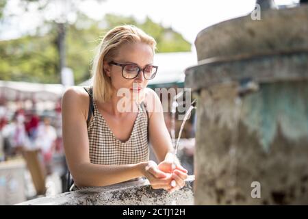 Durstige junge Casual cucasian Frau Trinkwasser aus der öffentlichen Stadt Brunnen an einem heißen Sommertag Stockfoto