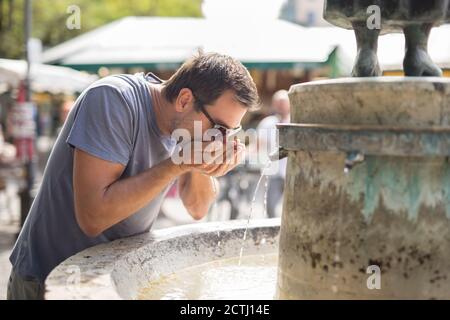Durstige junge Casual cucasian Mann Trinkwasser aus der öffentlichen Stadt Brunnen an einem heißen Sommertag Stockfoto