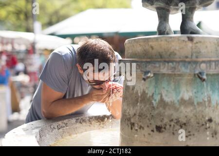 Durstige junge Casual cucasian Mann Trinkwasser aus der öffentlichen Stadt Brunnen an einem heißen Sommertag Stockfoto