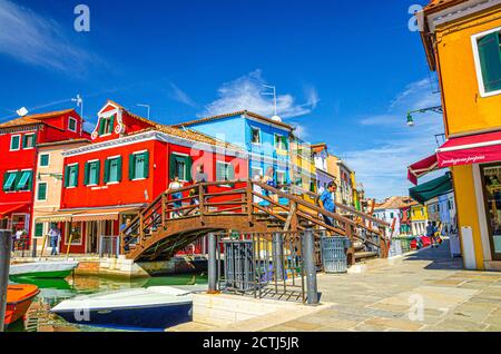 Burano, Italien, 14. September 2019: Menschen, die auf der Promenade in der Nähe von engen Wasserkanal mit bunten Häusern und Holzbrücke, blauer Himmel in sonnigen Sommertag Hintergrund, Provinz Venedig, Region Venetien Stockfoto