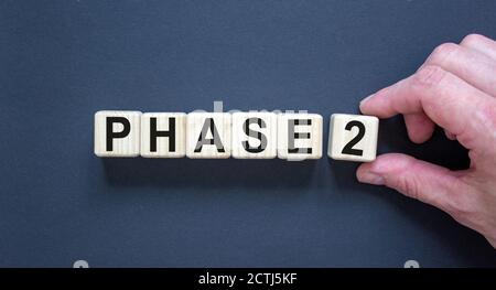 Zeit für Phase 2. Hand hält einen Würfel mit der Zahl '2'. Wort „Phase 2“. Schöner schwarzer Hintergrund. Geschäftskonzept. Speicherplatz kopieren. Stockfoto