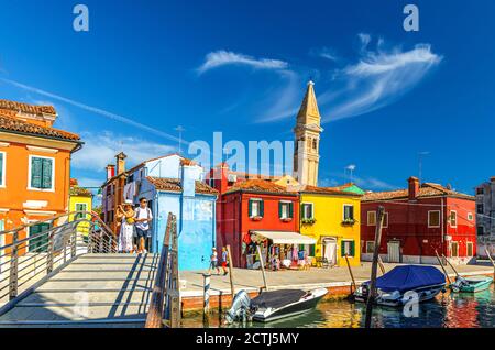 Burano, Italien, 14. September 2019: Bunte Häuser, Glockenturm der Kirche San Martino, Holzbrücke über den schmalen Wasserkanal mit Fischerbooten, Provinz Venedig, Region Venetien. Burano Postkarte Stockfoto