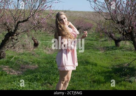 Schöne blonde Frau in rosafarbenem Kleid spaziert durch den blühenden Garten Stockfoto