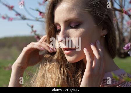 Schöne blonde Frau in rosafarbenem Kleid spaziert durch den blühenden Garten Stockfoto