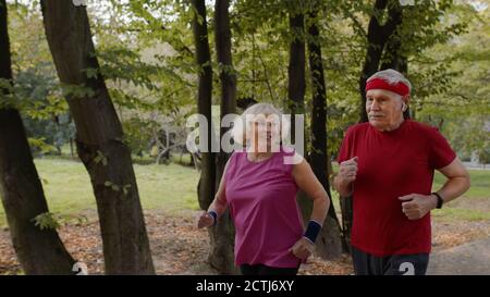 Fröhliches sportlich reifes Familienpaar joggt zusammen. Ältere Ehemann und Ehefrau machen Cardio-Workout-Übungen, laufen zusammen im Park. Freizeit Fitness Aktivität für Mann und Frau Stockfoto