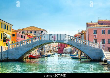 Steinbrücke Ponte di Vigo über den Kanal von Vena mit bunten Booten und alten Gebäuden im historischen Zentrum der Stadt Chioggia, blauer Himmel im Sommer, Region Venetien, Norditalien Stockfoto