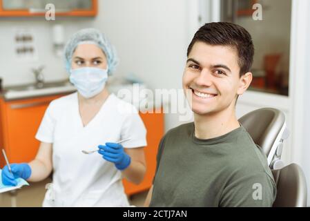 Zufriedener Patient auf dem Zahnarztstuhl. Der behandelnde Arzt steht hinter dem jungen Mann. Stockfoto